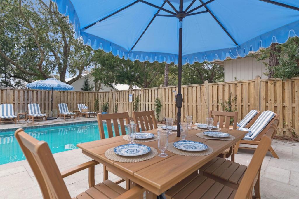 a wooden table with a blue umbrella next to a pool at Sunset Peak - 1928 Ocean Road in Saint Simons Island