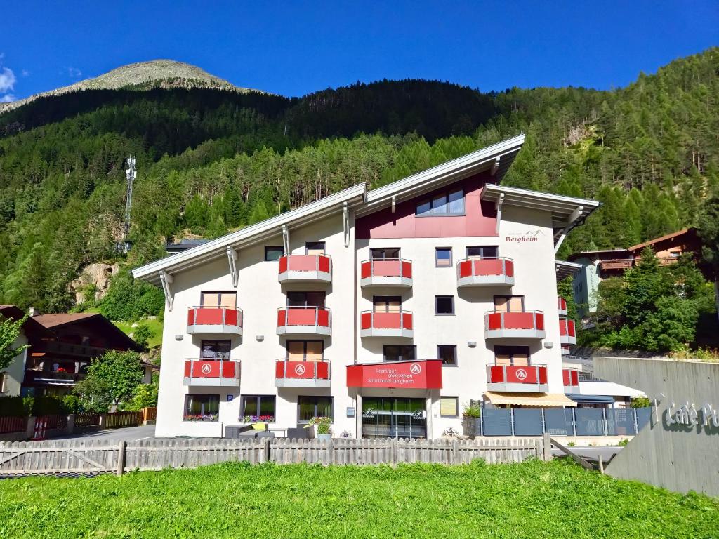 a building with red balconies in front of a mountain at Sporthotel Bergheim in Sölden