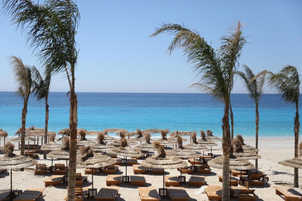 a beach with lounge chairs and palm trees and the ocean at Klodian Durmishi in Vlorë