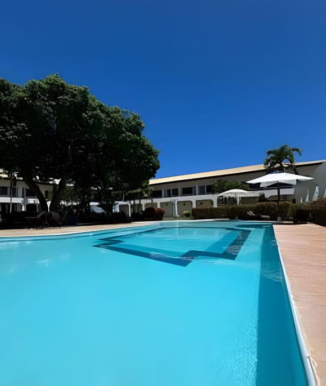 an empty swimming pool with an umbrella and a building at Guarajuba, apart 1/4 próximo à praia in Guarajuba