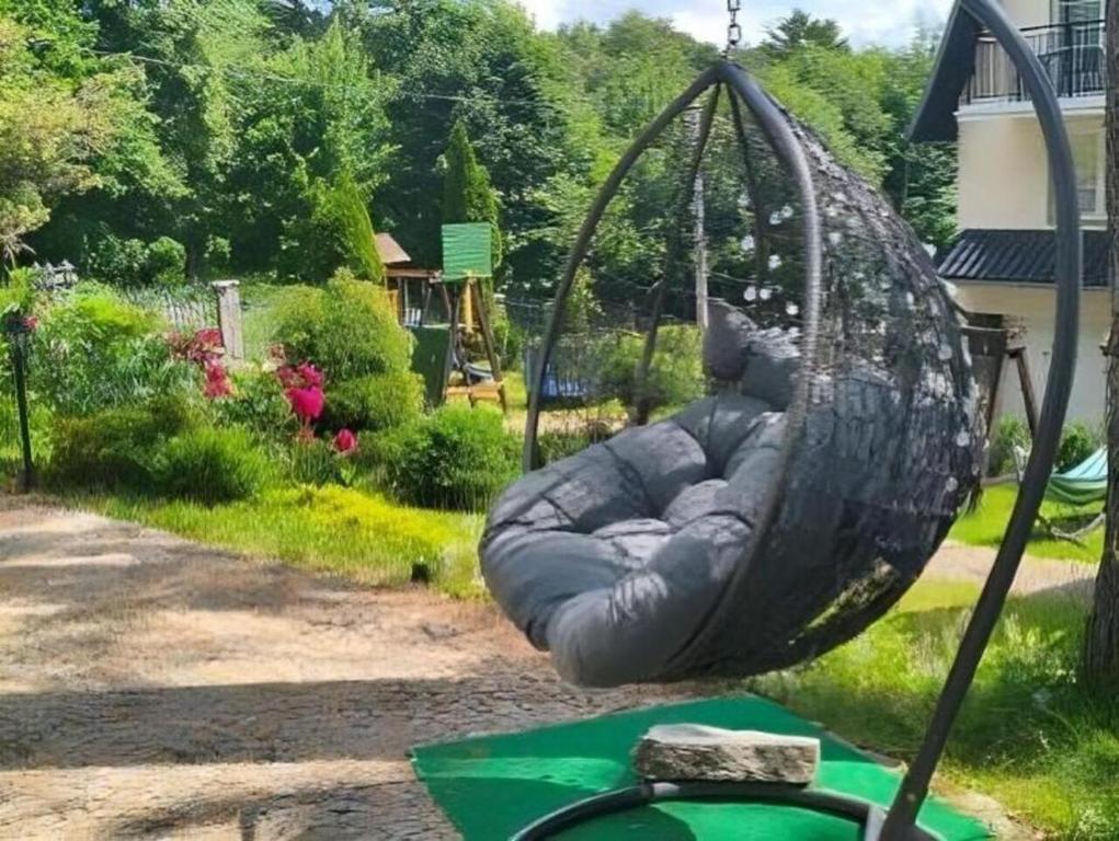 Hanging egg-shaped wicker chair with plush gray cushion suspended in green garden near children's playset.