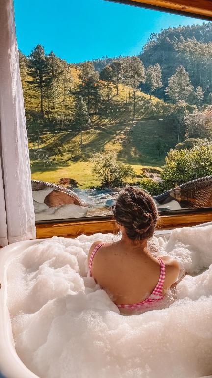 a woman sitting in a bath tub looking out a window at Refúgio do Vale Estalagem in Annitapolis