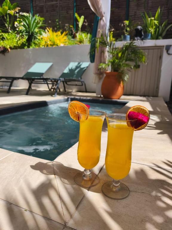 two glasses of orange juice sitting next to a swimming pool at Le SeaZen Lodge in Sainte-Anne