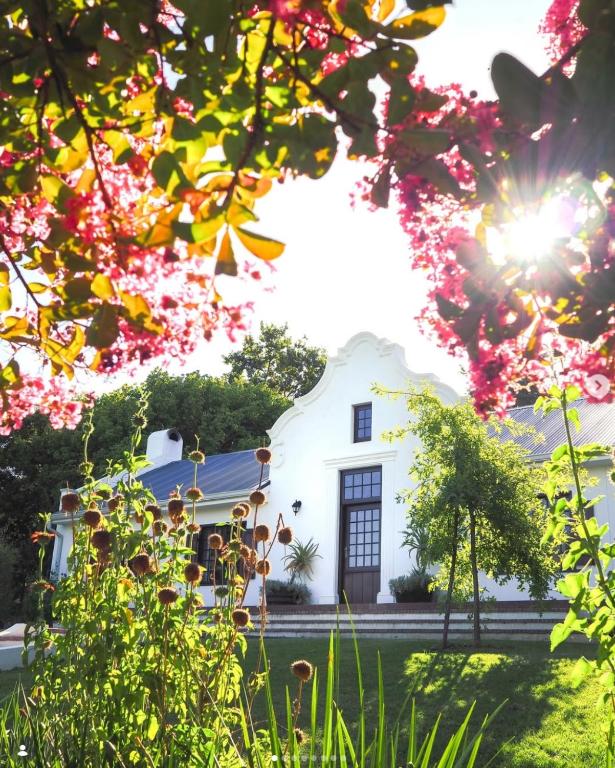 a white house with flowers in front of it at Plaisir Estate Accommodation in Simondium