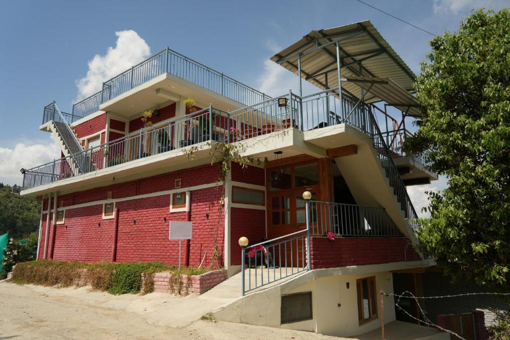 a red building with a balcony on top of it at The Windbloom - Himalayan Farm Stay in Mukteshwar