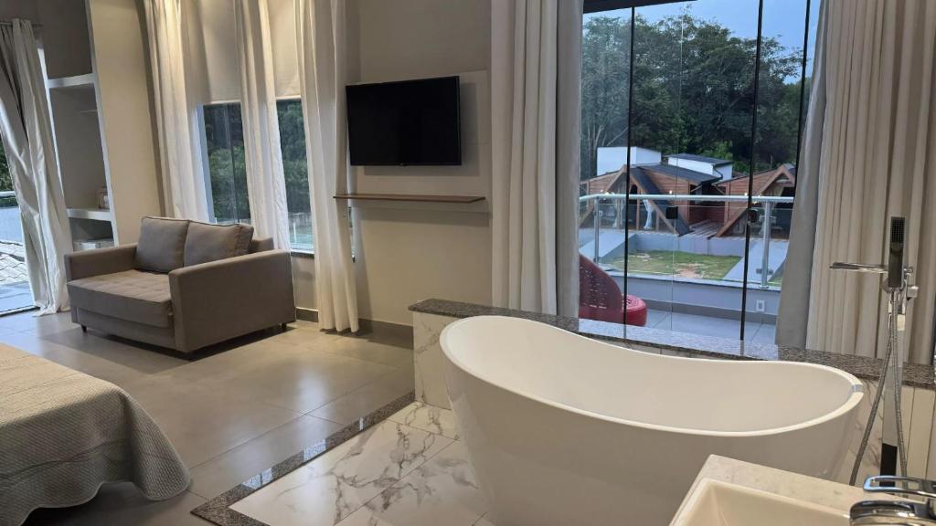 ein Badezimmer mit Badewanne, Stuhl und Fernseher in der Unterkunft AR Pousada in Santa Bárbara