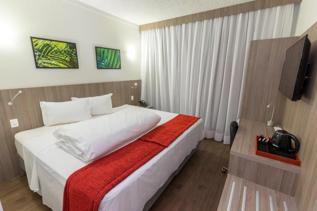 ein Schlafzimmer mit einem großen weißen Bett mit einer roten Decke in der Unterkunft Ramada by Wyndham Campinas Viracopos in Campinas