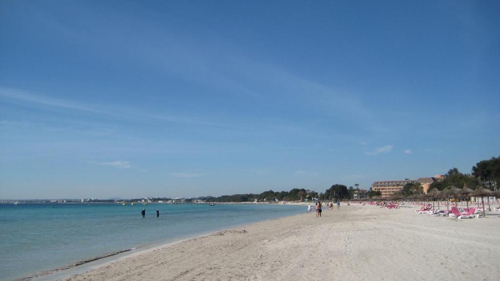 una playa con sillas y gente en la arena y el agua en Minerva Beach, en Puerto de Alcudia