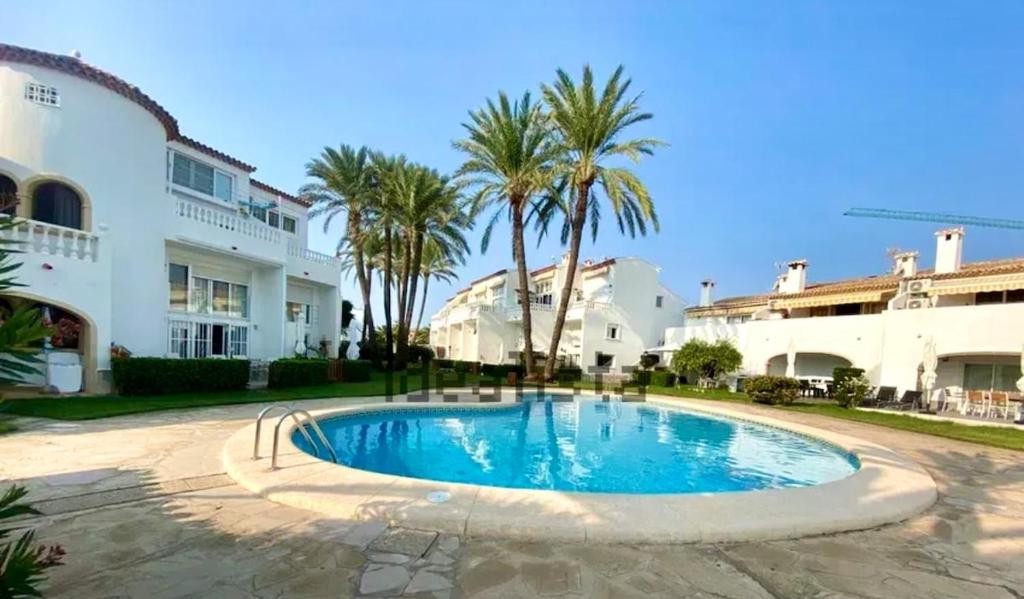 a swimming pool in front of a building with palm trees at Precioso bungalow con piscina en 1a Linea Playa in Denia
