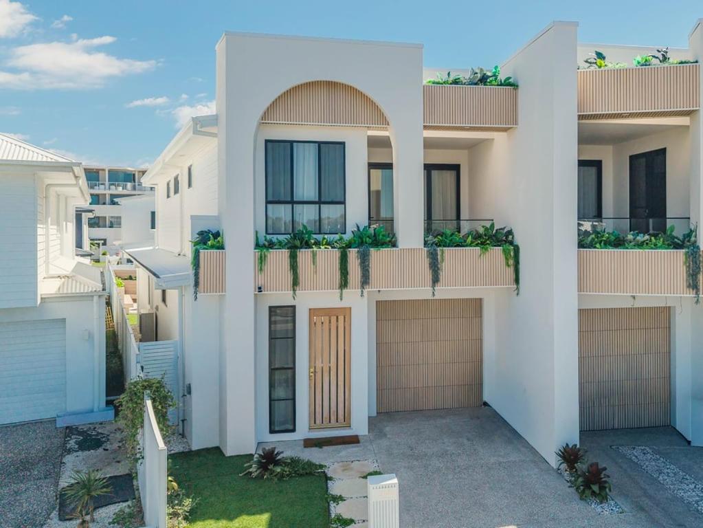 a white house with a brown door and some buildings at Black Wattle Beach House in Casuarina