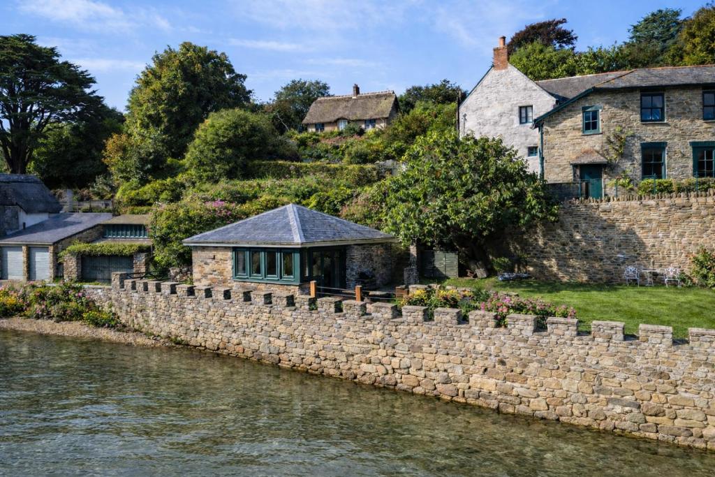 a stone wall next to a river with houses at The Boathouse - Salcombe - Spring Time Tiny Home in Salcombe