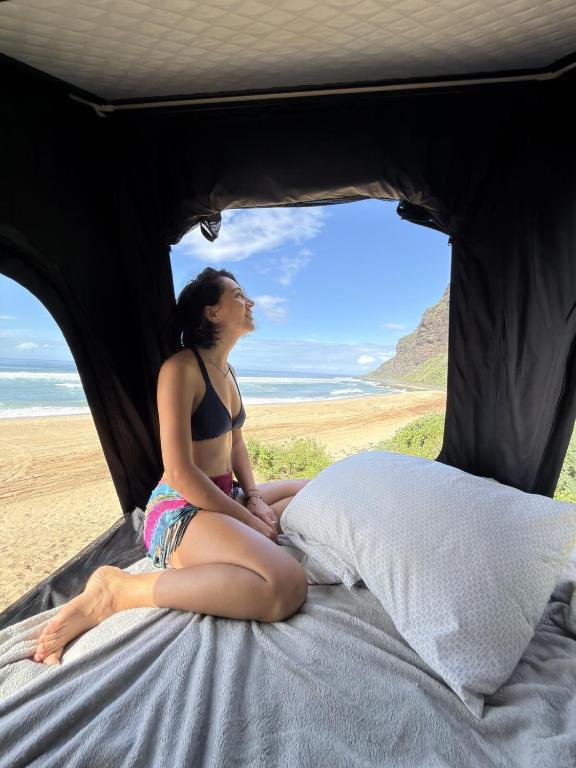 a woman sitting on a bed on the beach at Kauai Explorer Camp Rooftop Camper fully equipped in Anahola