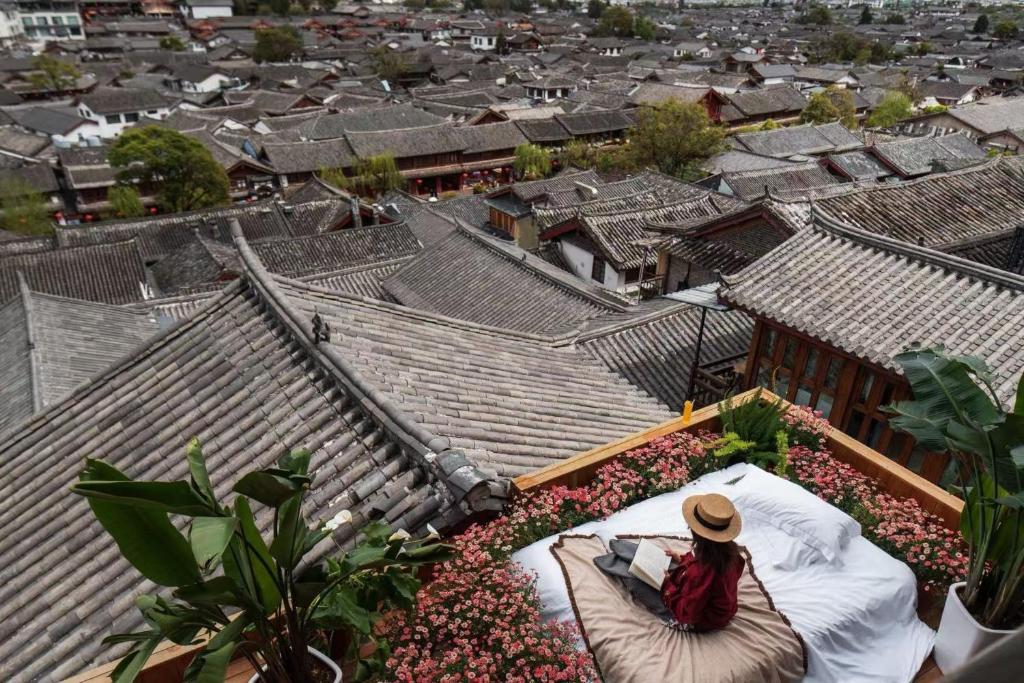 a woman sitting on a bed on top of a city at Maison lyly 300 Year Historical Cultural Courtyard and Ancient City View in Lijiang