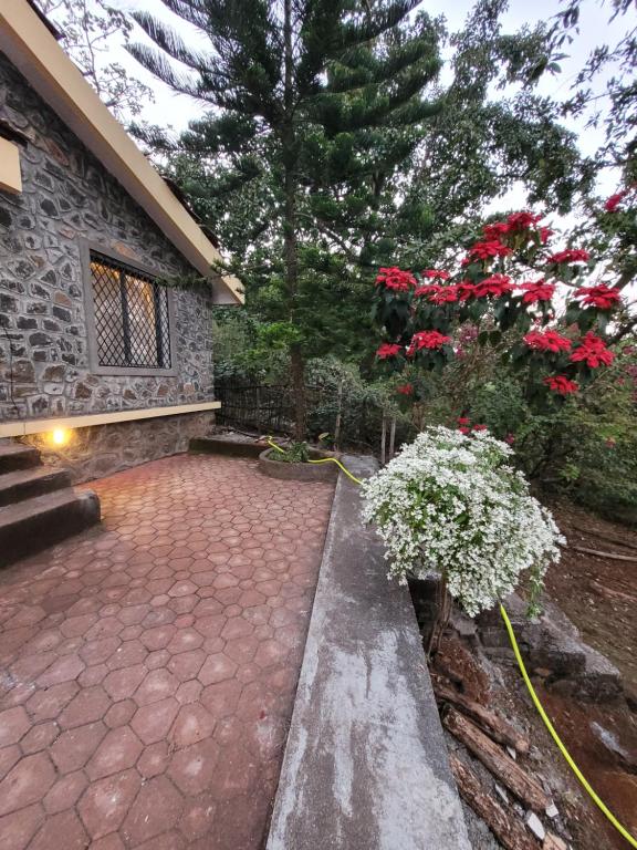 a patio with red flowers and a stone building at Alhaad valley views in Mulshi