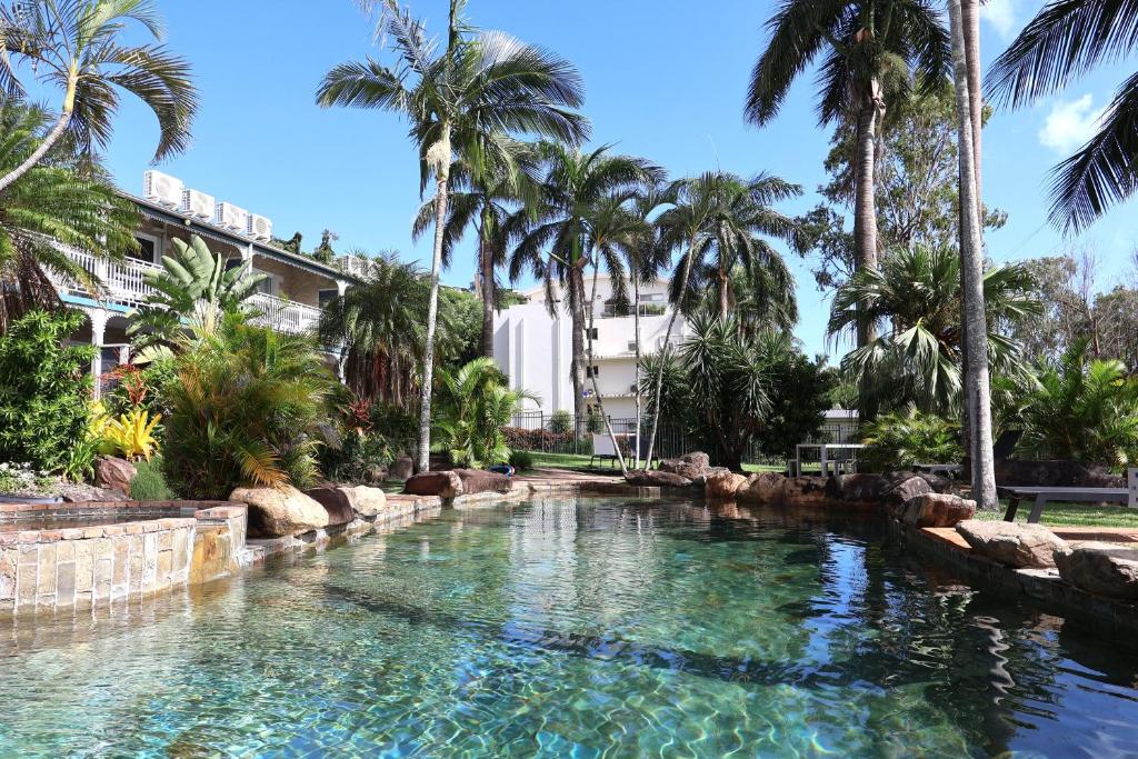 a swimming pool with palm trees in a resort at Colonial Palms Motor Inn in Airlie Beach