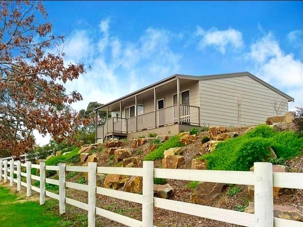 a house on top of a hill with a fence at Oak Hill Cottage - Chirnside Park in Wonga Park