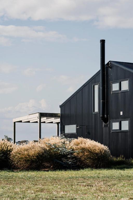 a black building in a field with tall grass at Connewarre Farm Stay - Sleeps 10 - Acreage By HostyCo in Connewarre