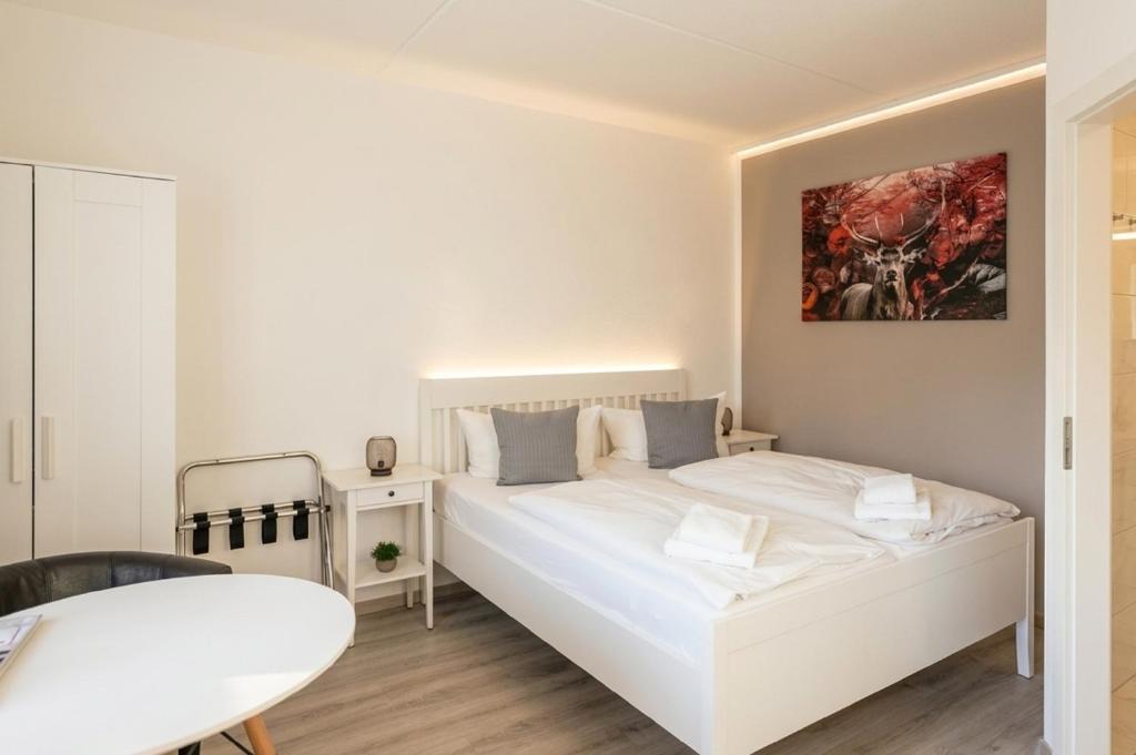 a white bedroom with a bed and a table at REGIOHOTEL Wolmirstedter Hof in Wolmirstedt