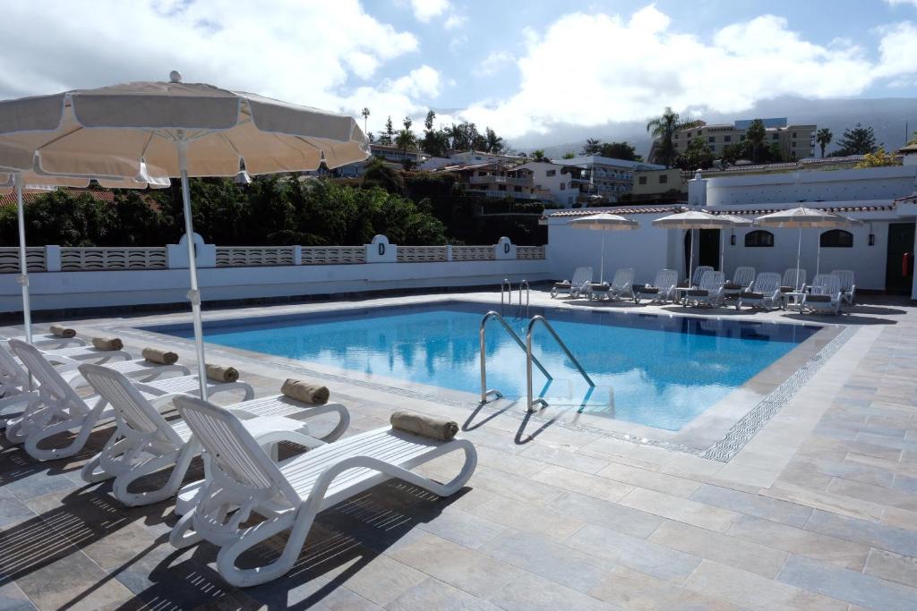a swimming pool with white chairs and an umbrella at Muthu La Perla Tenerife in Puerto de la Cruz