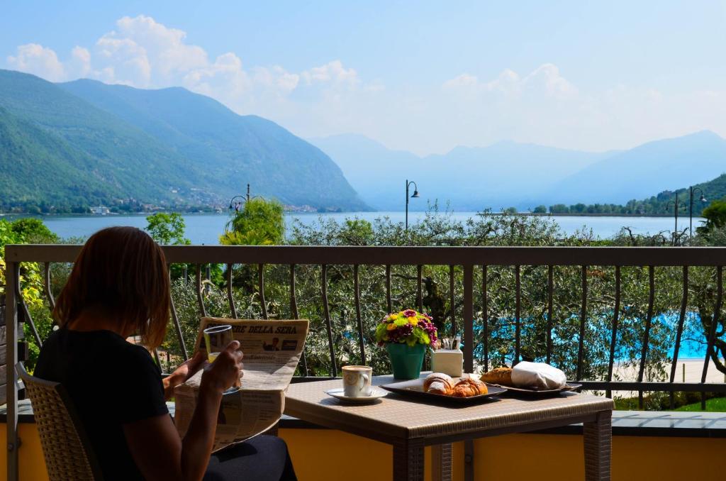 una donna seduta a un tavolo sul balcone leggendo un libro di Hotel Ulivi a Paratico