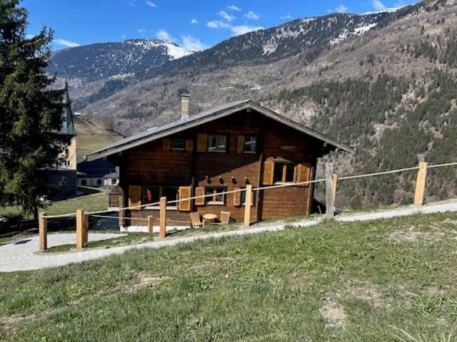 a wooden cabin in a field with a mountain at Swiss Chalet - upstairs apartment in Grengiols