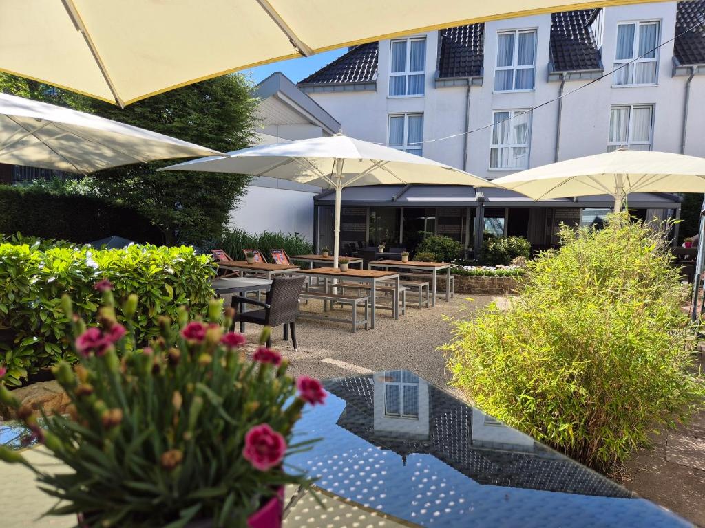 eine Terrasse mit Tischen und Sonnenschirmen vor einem Gebäude in der Unterkunft Ringhotel Appelbaum Gütersloh in Gütersloh