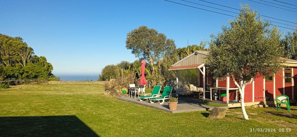 a red house with green chairs and a yard at Cabana Papoila in Colares