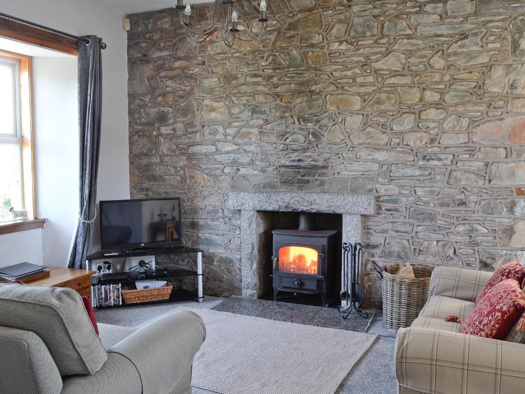 a living room with a stone wall with a fireplace at Horsepark Cottage in Girthon