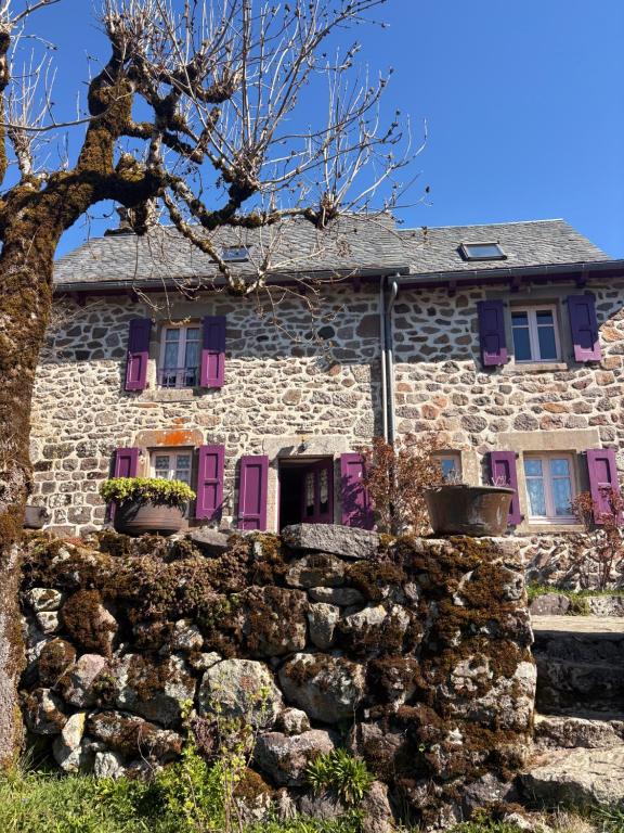 an old stone house with purple shutters and a stone wall at Nouveau - Maison Nierveze proche Lioran in Thiézac