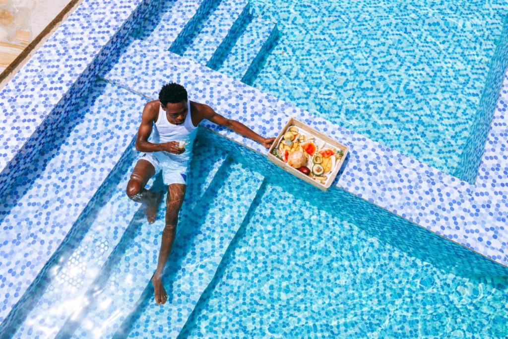 a man in a swimming pool with a box of food at Farashuu Luna Hotel in Kendwa