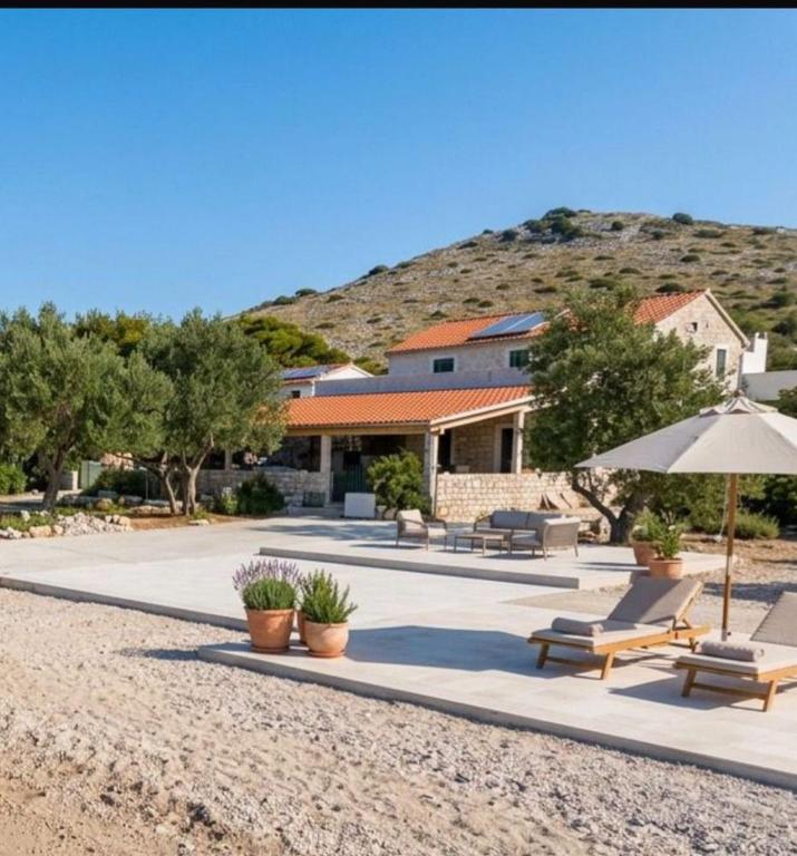 a house with benches and an umbrella on a beach at Seafront Villa in Kornati Private Terrace and Direct Beach Access in Kornati