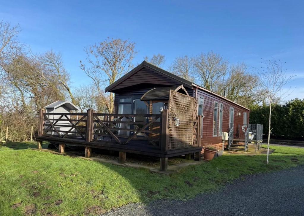 a large wooden cabin with a porch in the grass at Two Bedroom Lodge in Gainsborough