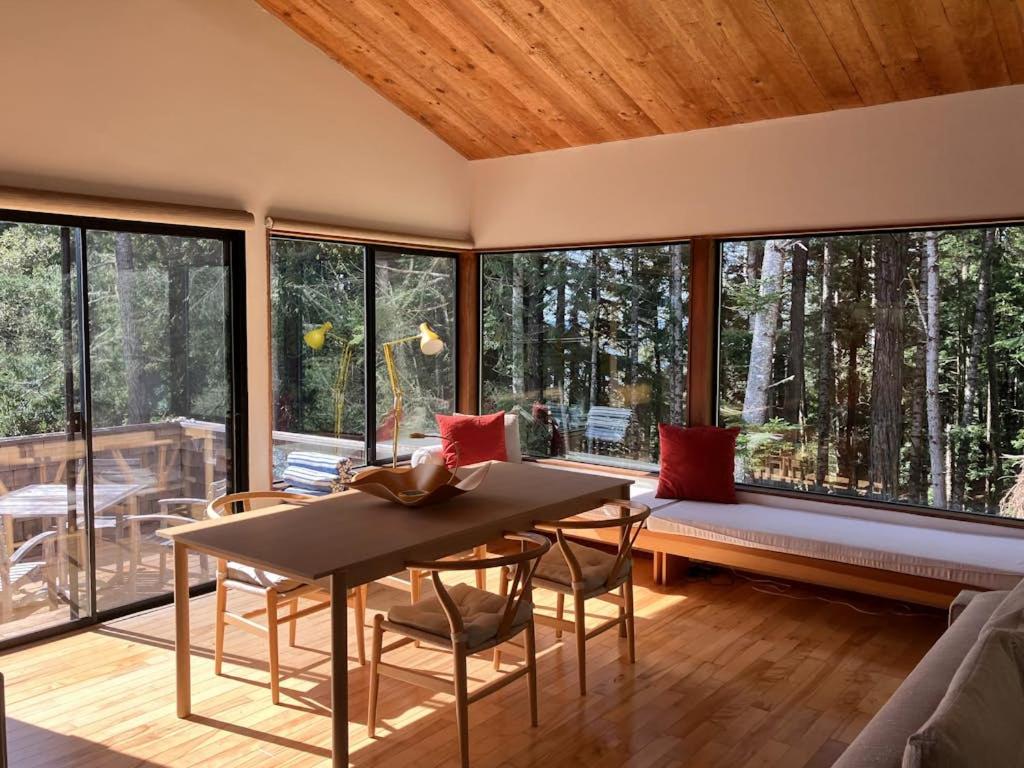 a living room with a table and chairs and windows at Madrone Meadow in Sea Ranch