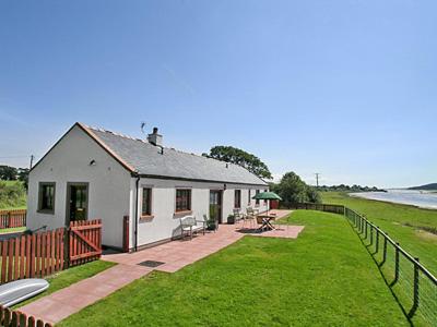 a small white house with a fence next to the water at Martha's Shore Cottage in Glencaple