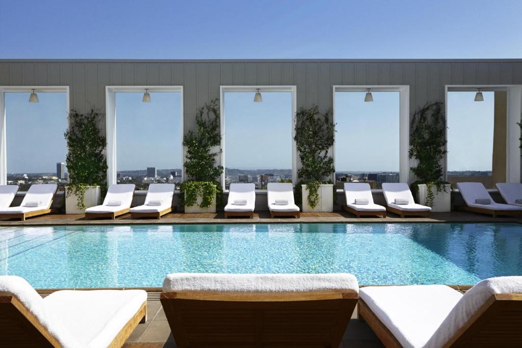 ein Schwimmbad mit weißen Liegestühlen in einem Gebäude in der Unterkunft The Valorian Los Angeles, Curio Collection by Hilton in Los Angeles