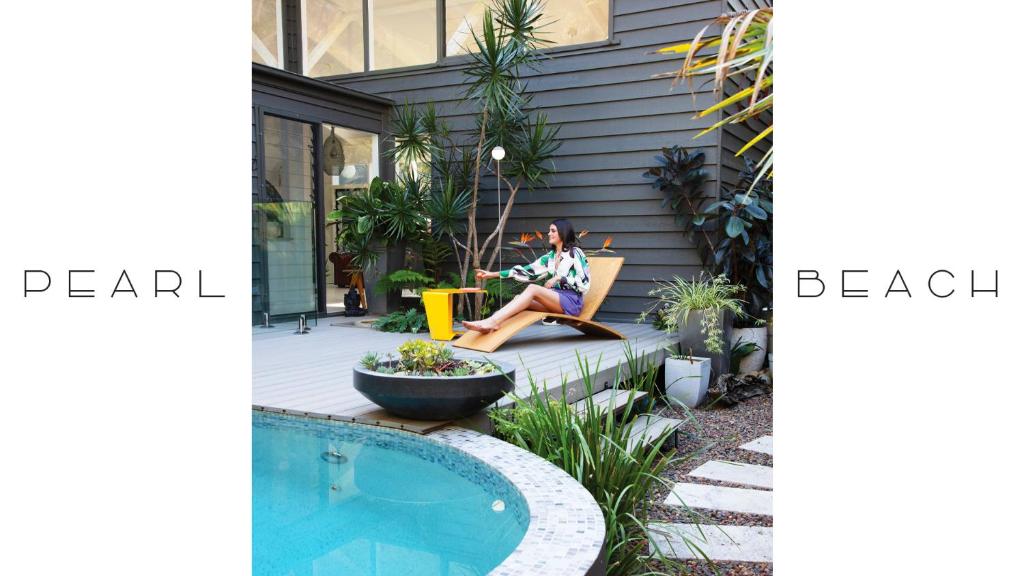 a woman sitting in a chair next to a house at Luxury Pearl Beach House with Private Heated Mineral Pool, Yoga Deck & Fire Pit in Pearl Beach