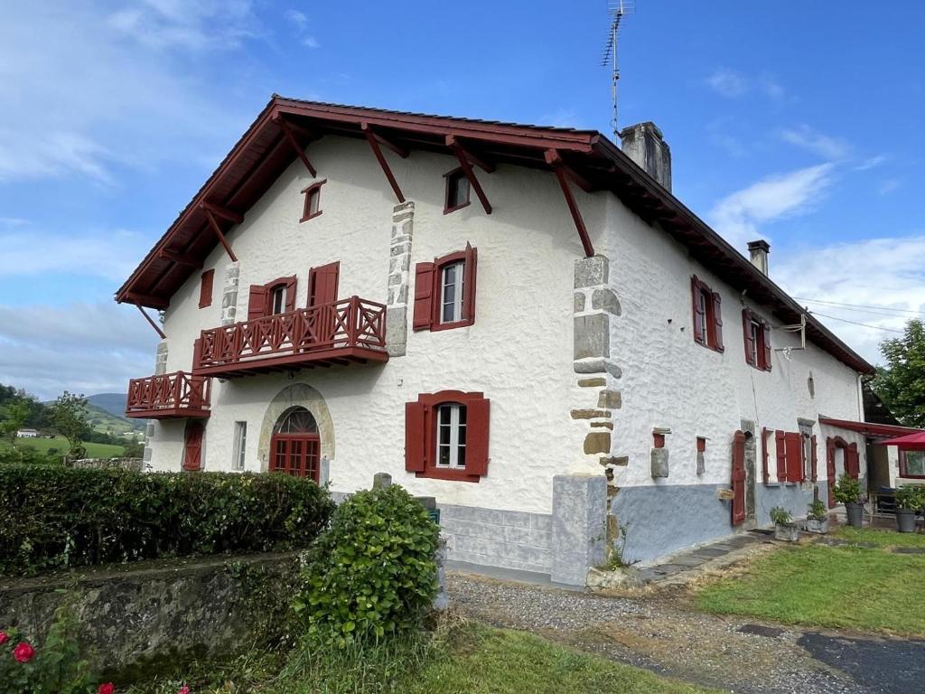 a white house with red windows and a balcony at Chambre argoitzia in Saint-Martin-dʼArberoue