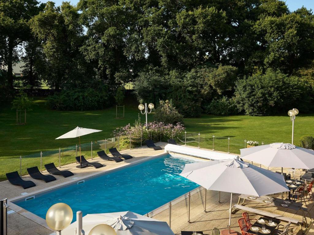 a swimming pool with chairs and umbrellas at Novotel Bayeux in Bayeux