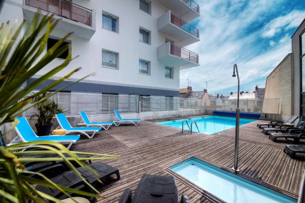 a patio with chairs and a swimming pool on a building at Comfort Aparthotel Saint-Nazaire Les Portes de l Ocean in Saint-Nazaire