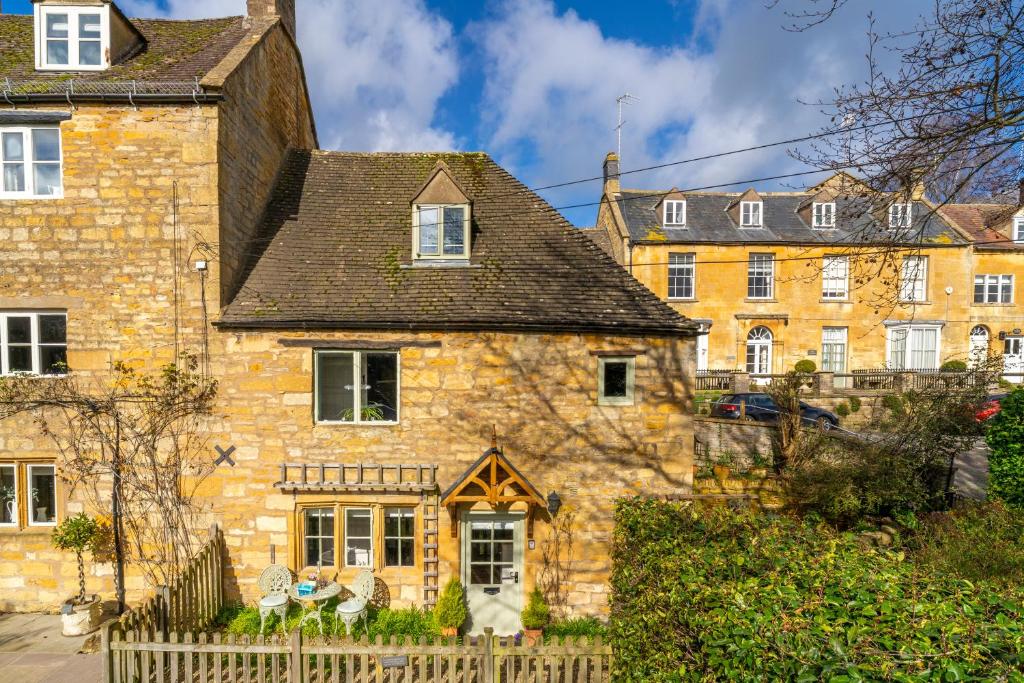 an old stone house with a fence in front of it at 4 Crown Cottages in Moreton in Marsh