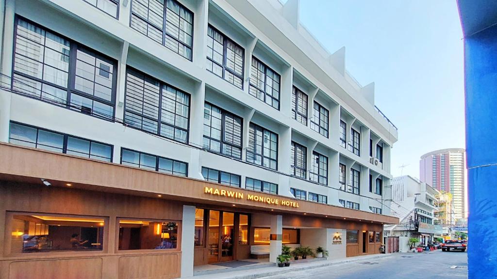 a large white building with windows on a city street at Marwin Monique Hotel in Bangkok