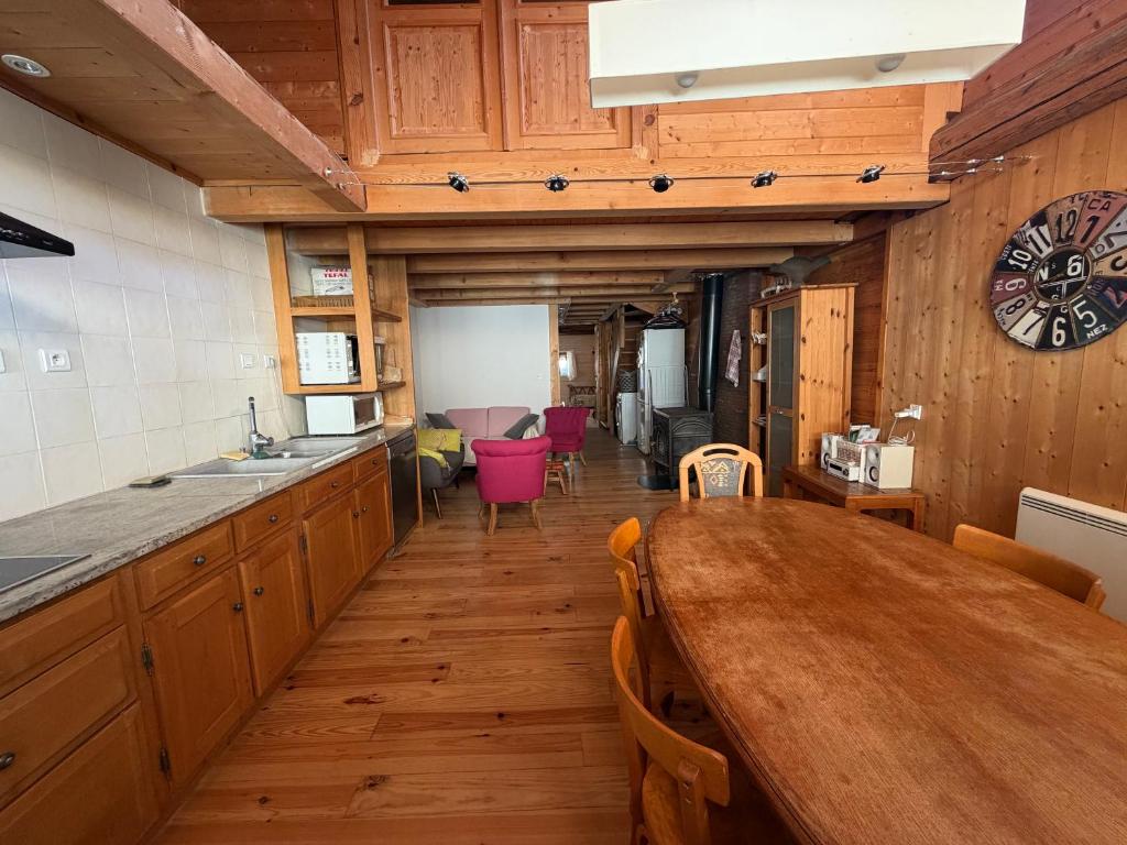 a kitchen with a long wooden table and a clock on the wall at La Marguerite in Aigueblanche