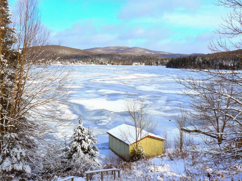a small building in the snow next to a lake at Chalet Le Pélican in Lac-Superieur