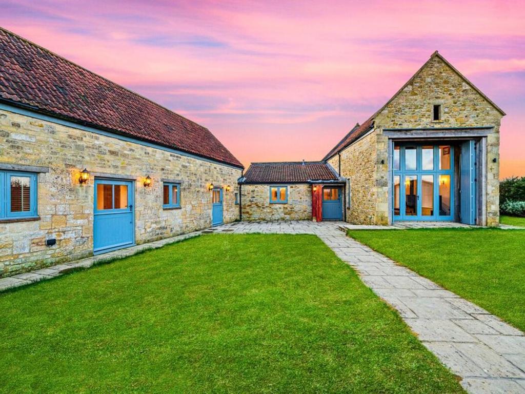an old stone house with blue doors and a grass yard at Knoll View Ranch in Shepton Mallet