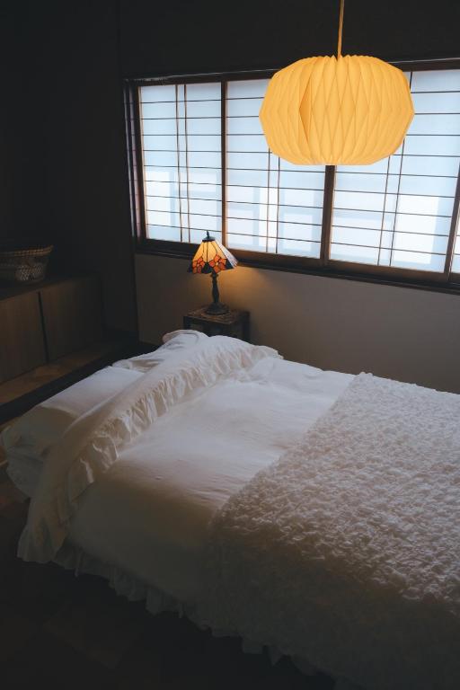 a bedroom with a white bed with a lamp and a window at ゲストハウス レトロマチカ in Sakai