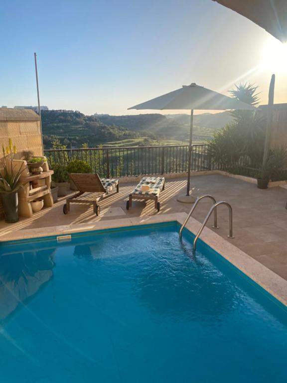 a swimming pool with benches and an umbrella at Ta’ Giljan B&B Gozo in Xagħra