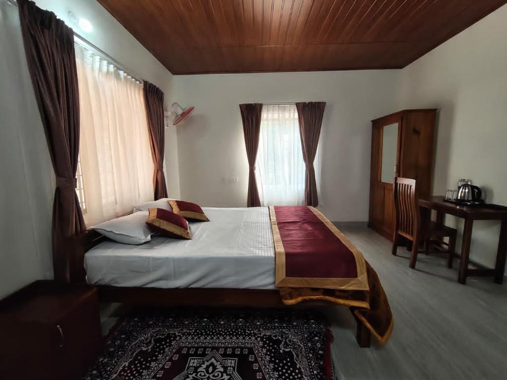 a bedroom with a bed with a desk and windows at Riverwood Cottages in Kallar Vattiyar