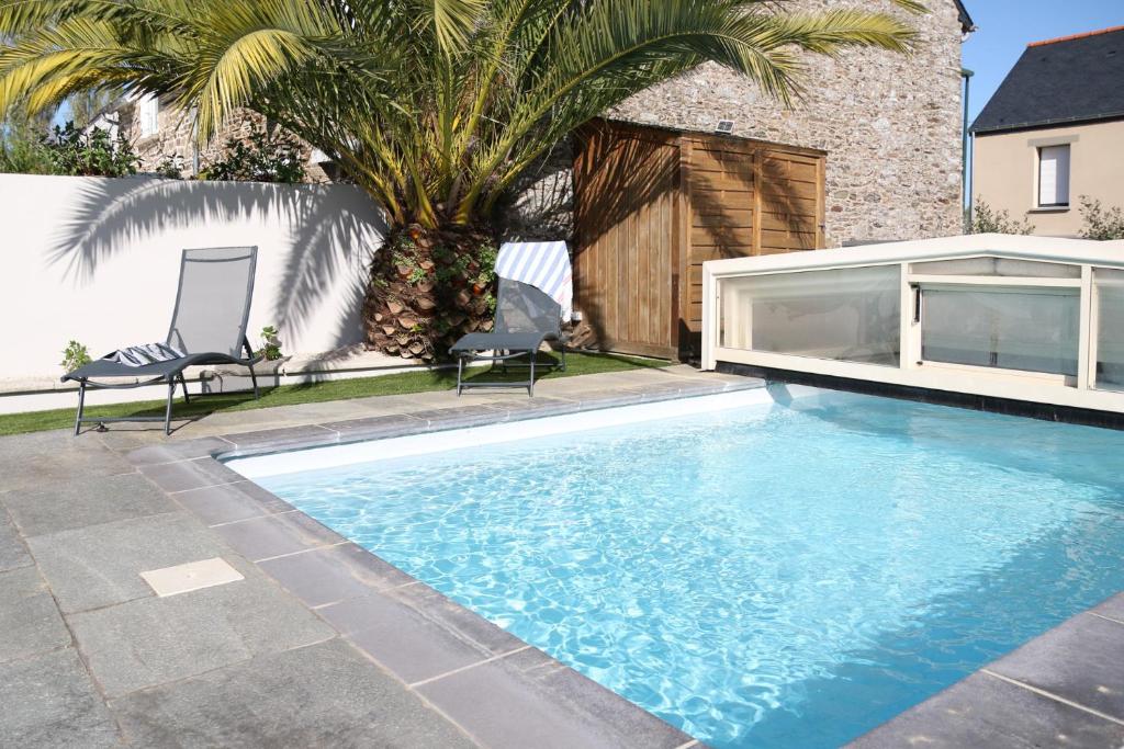 a swimming pool with two chairs and a palm tree at Azur Cancale in Cancale