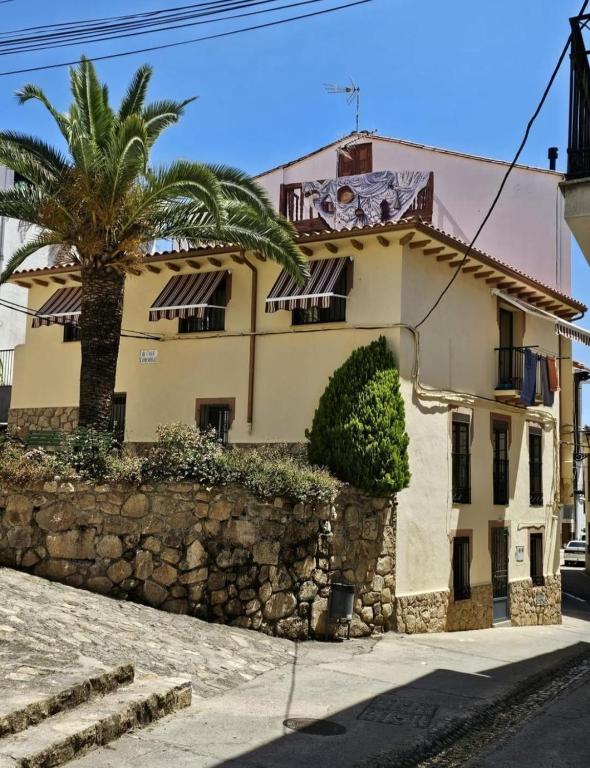 a building with a palm tree next to a stone wall at Casa Rural La Changa in Losar de la Vera