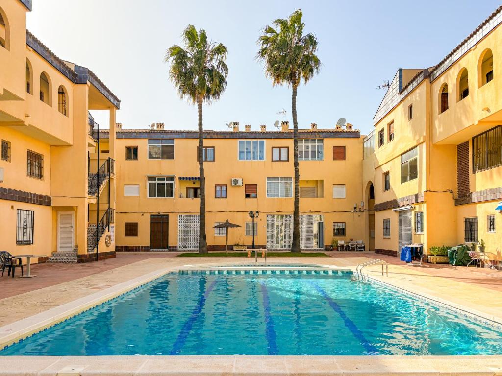 a swimming pool in front of a building with palm trees at SiCasa Punta Prima in Punta Prima